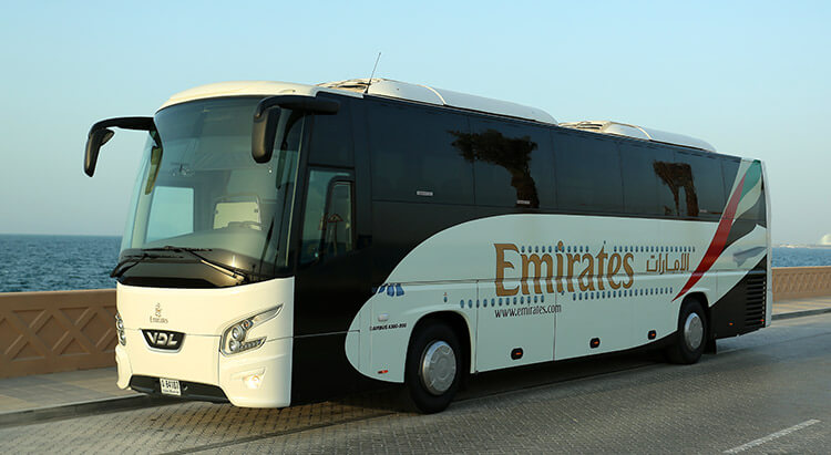 A modern luxury bus parked in front of the iconic Burj Khalifa in Dubai, ready for passenger boarding.